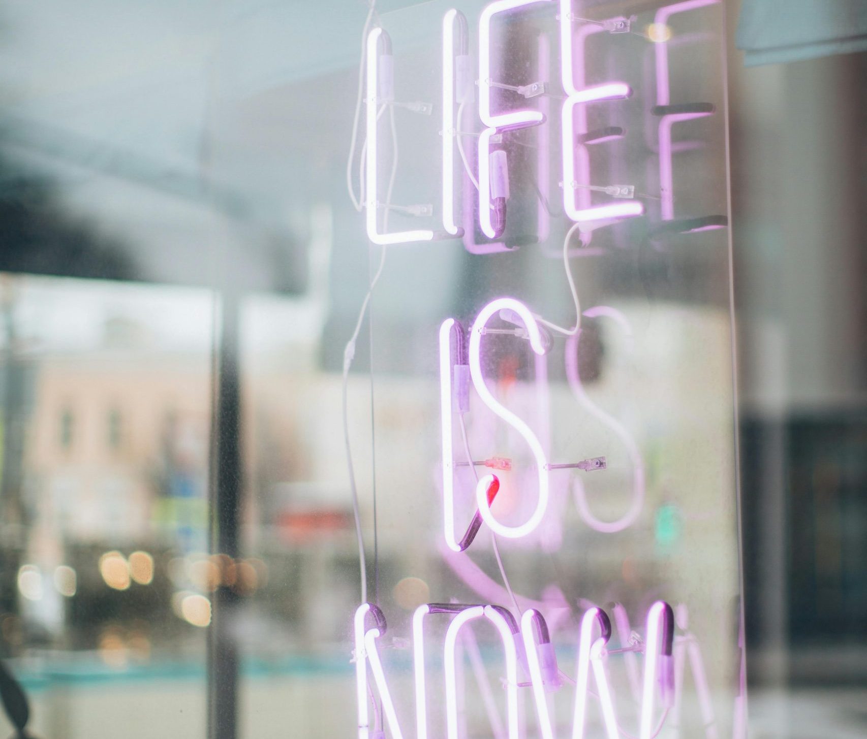 Urban scene with a glowing 'Life is Now' neon sign reflecting in a window, conveying a modern, motivational vibe.
